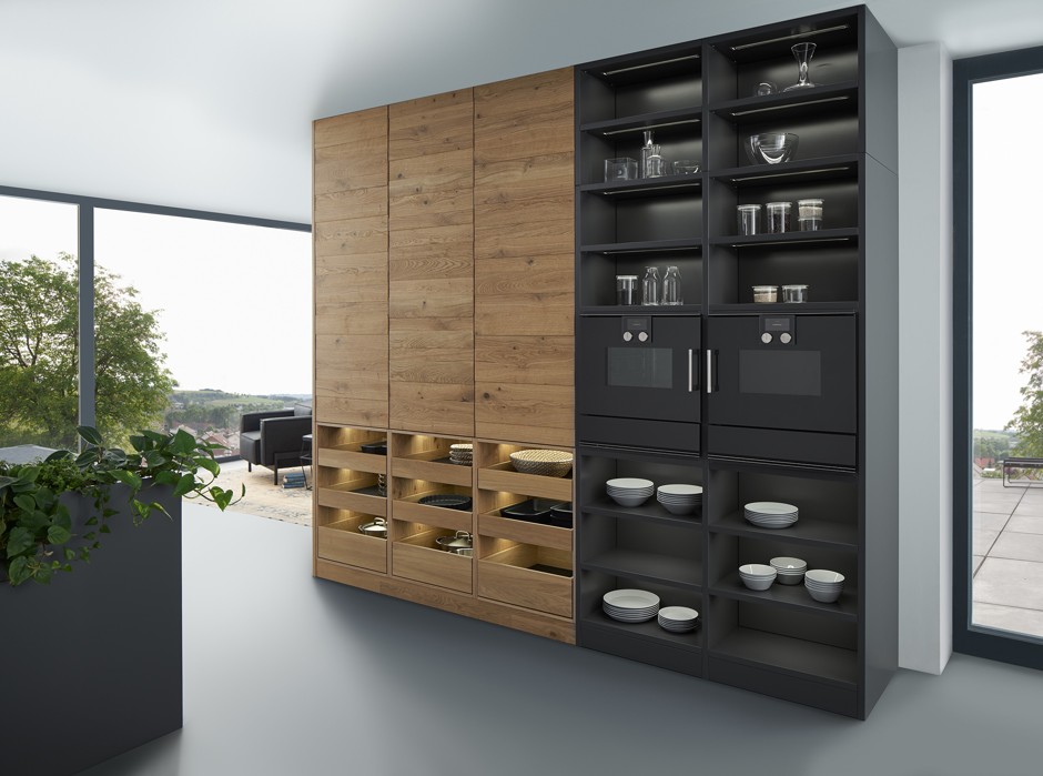 Die Küchen werden gemütlicher und wachsen mit dem Wohnzimmer zusammen. Dabei spielen auch dunkle Töne in der Kombination mit Holzoptik eine große Rolle. (Foto: AMK)