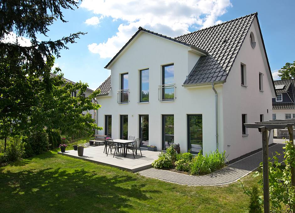 Blick vom Garten auf Terrasse und Rückseite des anderthalbgeschossigen Gebäudes. Bo-dentiefe Fenster erweitern den Wohnbereich ins Grüne. Fotos: HELMA Eigenheimbau AG / Christoph Große