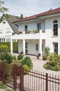 Ein auf Pfeilern ruhender Eingangsbereich, Rundbogenfenster mit Sprossen und die Dachlandschaft verleihen der Stadtvilla Urlaubsflair. Foto: Roth-Massivhaus / Gerhard Zwickert