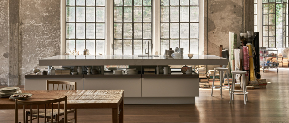 Wohnküchen – lebenssprühend sinnanregend. Die Kücheninsel fasziniert durch Kontraste: ein symmetrisch-asymmetrisches Design sowie geschlossene und offene Bereiche mit ausziehbaren Holztablaren. Foto: AMK