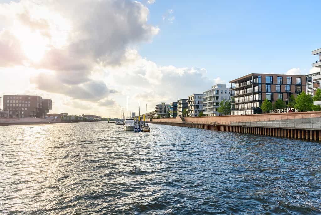 Neue Wohnhäuser in einem sanierten Gebiet entlang eines ehemaligen Flusshafens bei Sonnenuntergang. In der Mitte des Hafens sind Boote zu sehen, die an einem Steg festgemacht haben. Bremen, Deutschland.