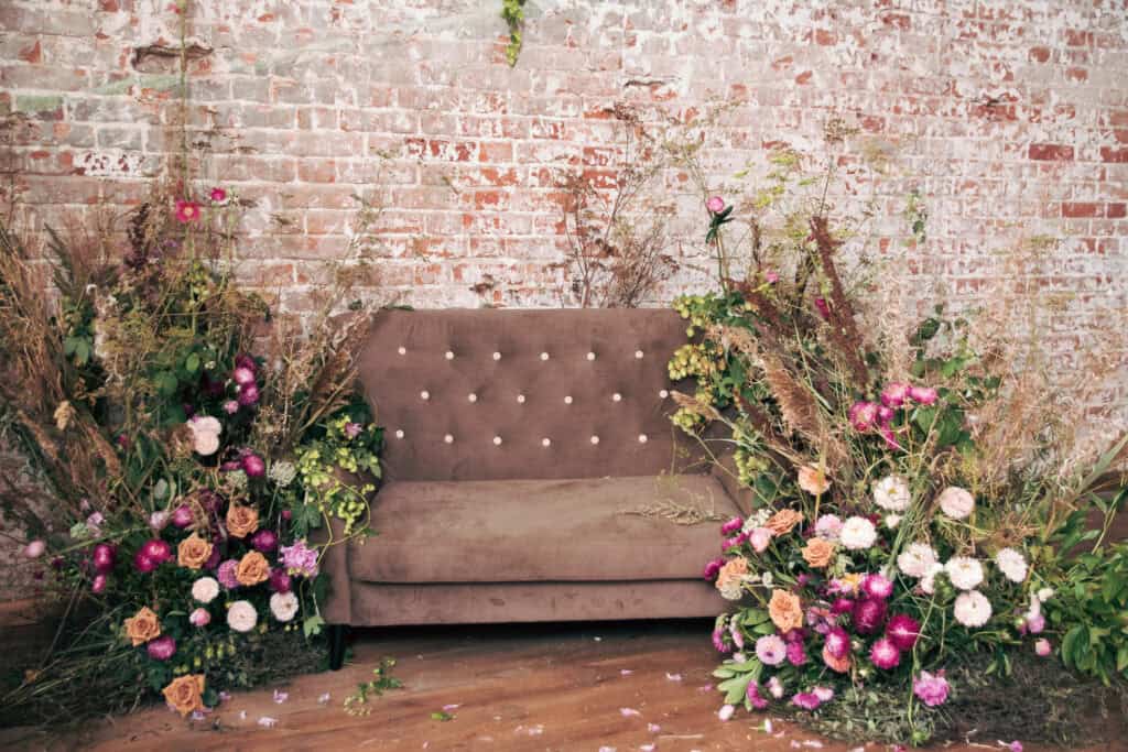 Luxus-Sofa mit getrockneten Blumen, Rosen, Weizen in der Nähe. Schönes Interieur auf einem roten Backstein Hintergrund.